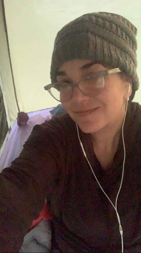 This photo shows a selfie Priscilla took. She is smiling, wearing glasses and a grey beanie. Her earpod headphones are visible, too. She is wearing a dark red long sleeved shirt.